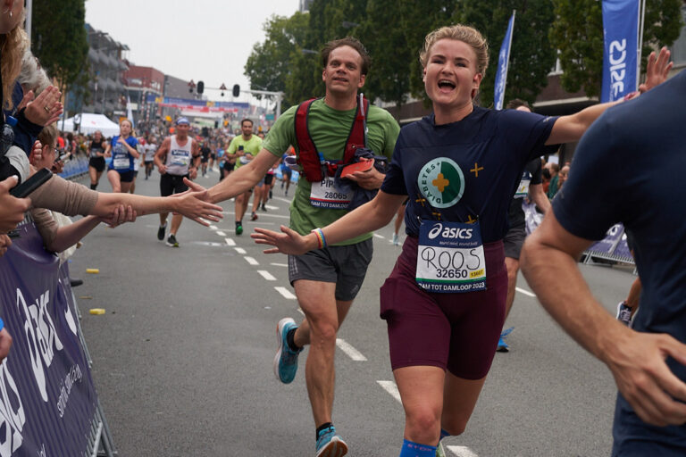 Vrouw en man komen over de finish van een hardloopwedstrujd. Vrouw draagt DiabetesPlus shirt