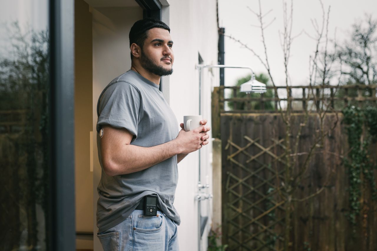 Man met donker haar en baard met een beker koffie. Hij draagt een Medtronic insulinepomp aan zijn riem